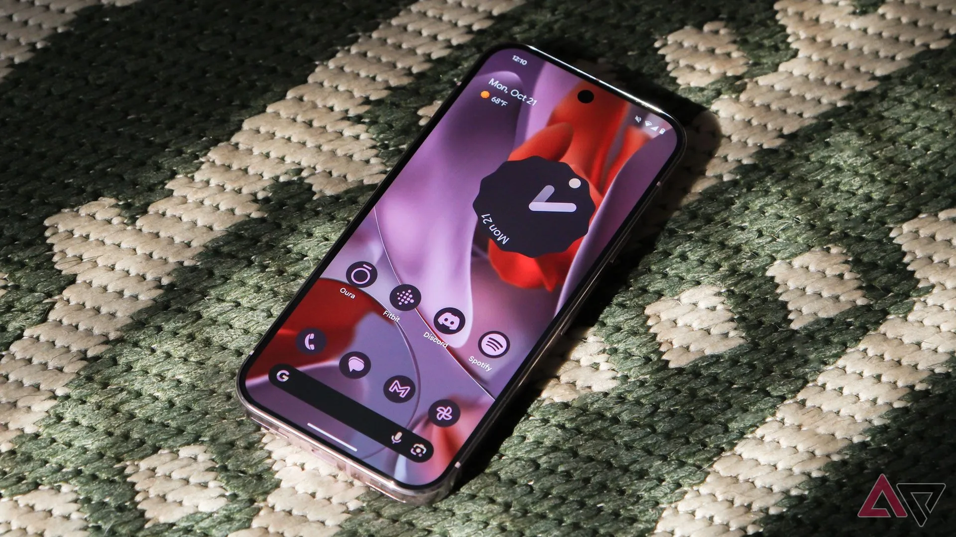 Google Pixel 9 Pro đặt ngửa trên thảm màu xanh lá cây, màn hình hiển thị màn hình chính Android 15.