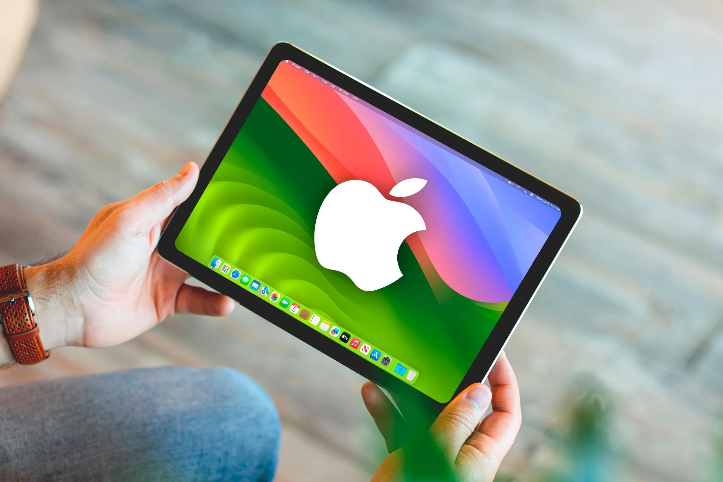 Một bàn tay cầm iPad hiển thị logo macOS và Apple trên màn hình, minh họa ý tưởng (sai lầm) về việc chạy macOS trên iPad.