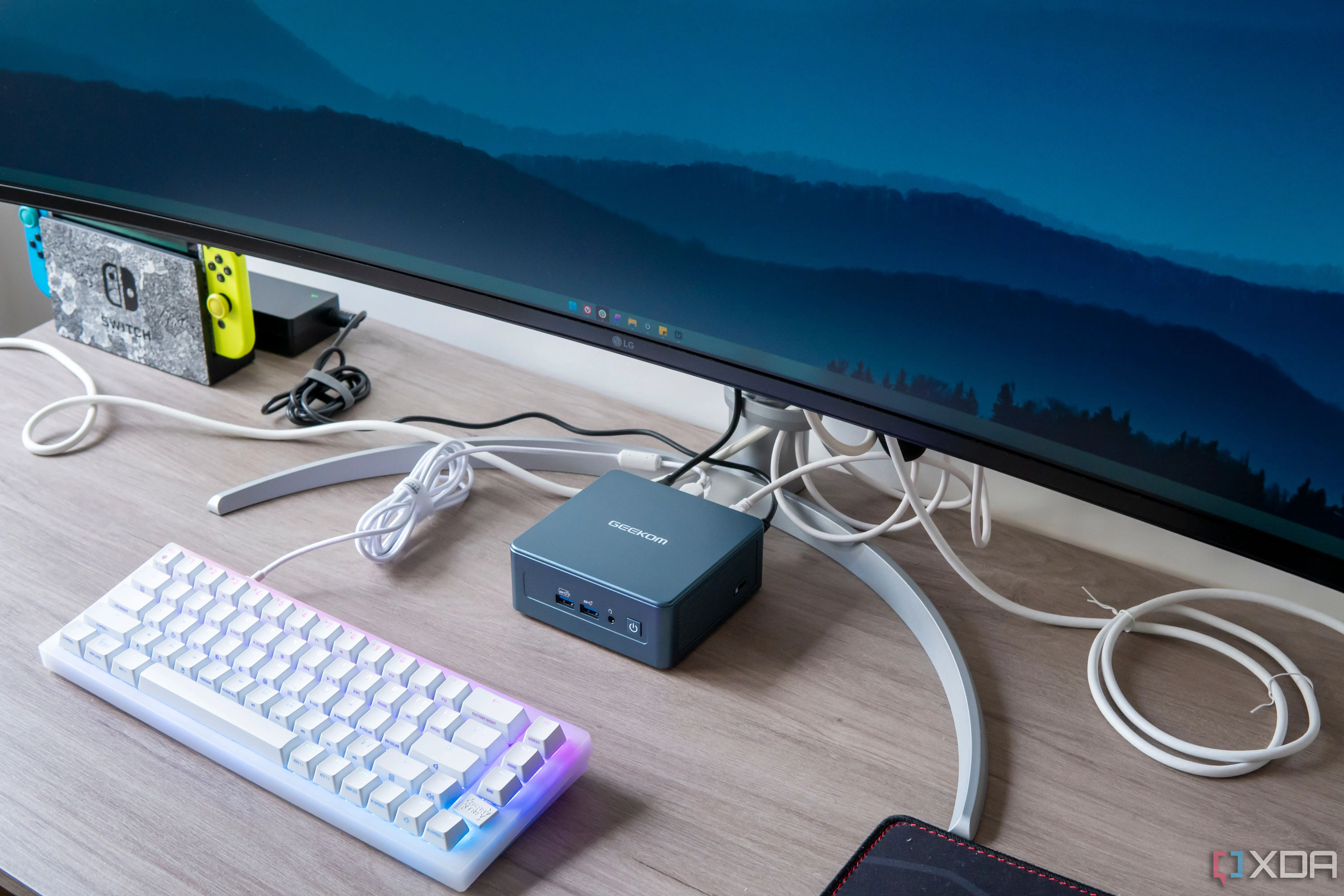 Máy tính mini Geekom Mini IT13 đặt dưới màn hình, tượng trưng cho đa dạng phần cứng hỗ trợ Windows.