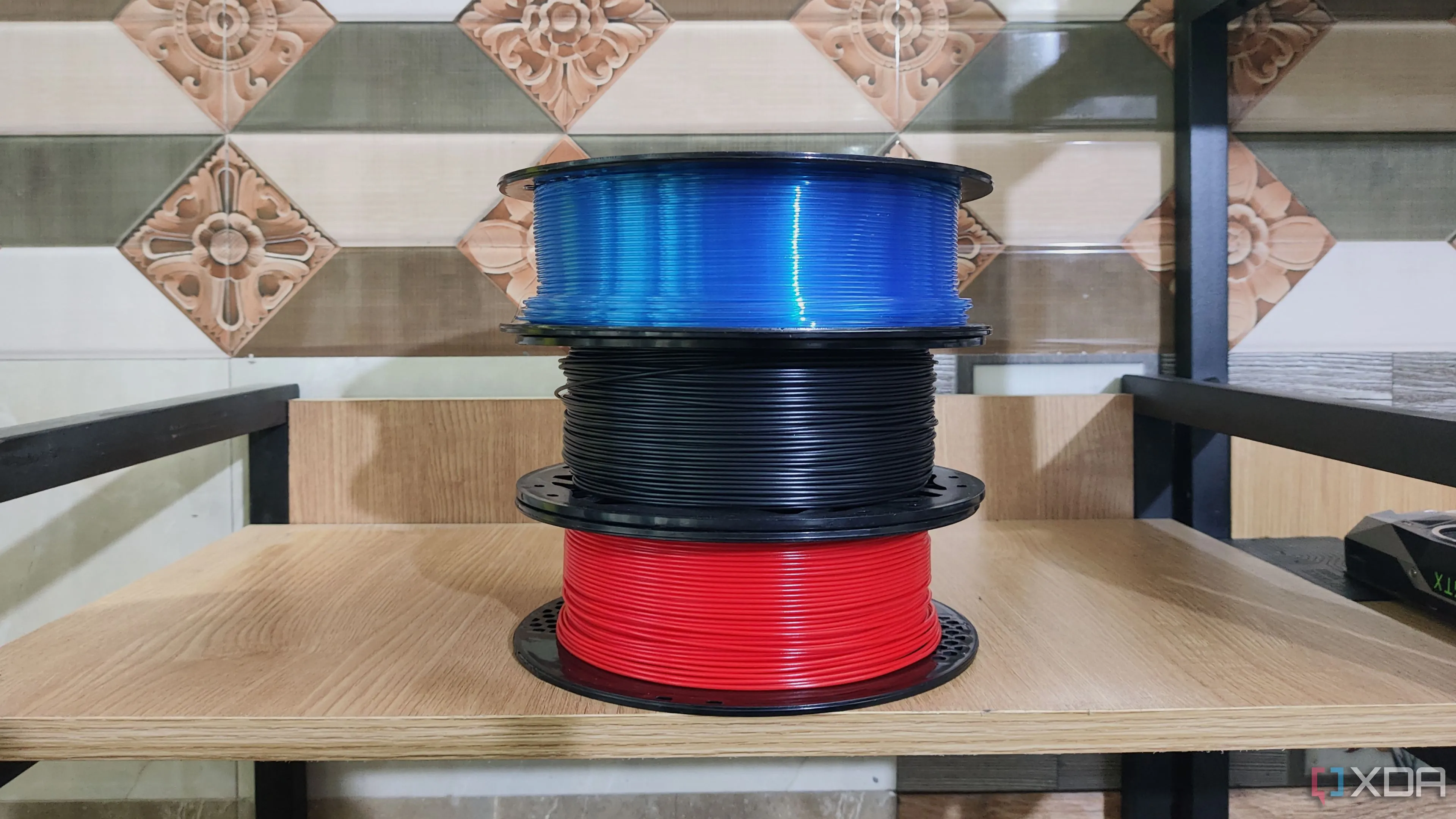 Ba cuộn filament với các kích cỡ khác nhau đặt cạnh máy in 3D, thể hiện sự cần thiết của giá đỡ lớn