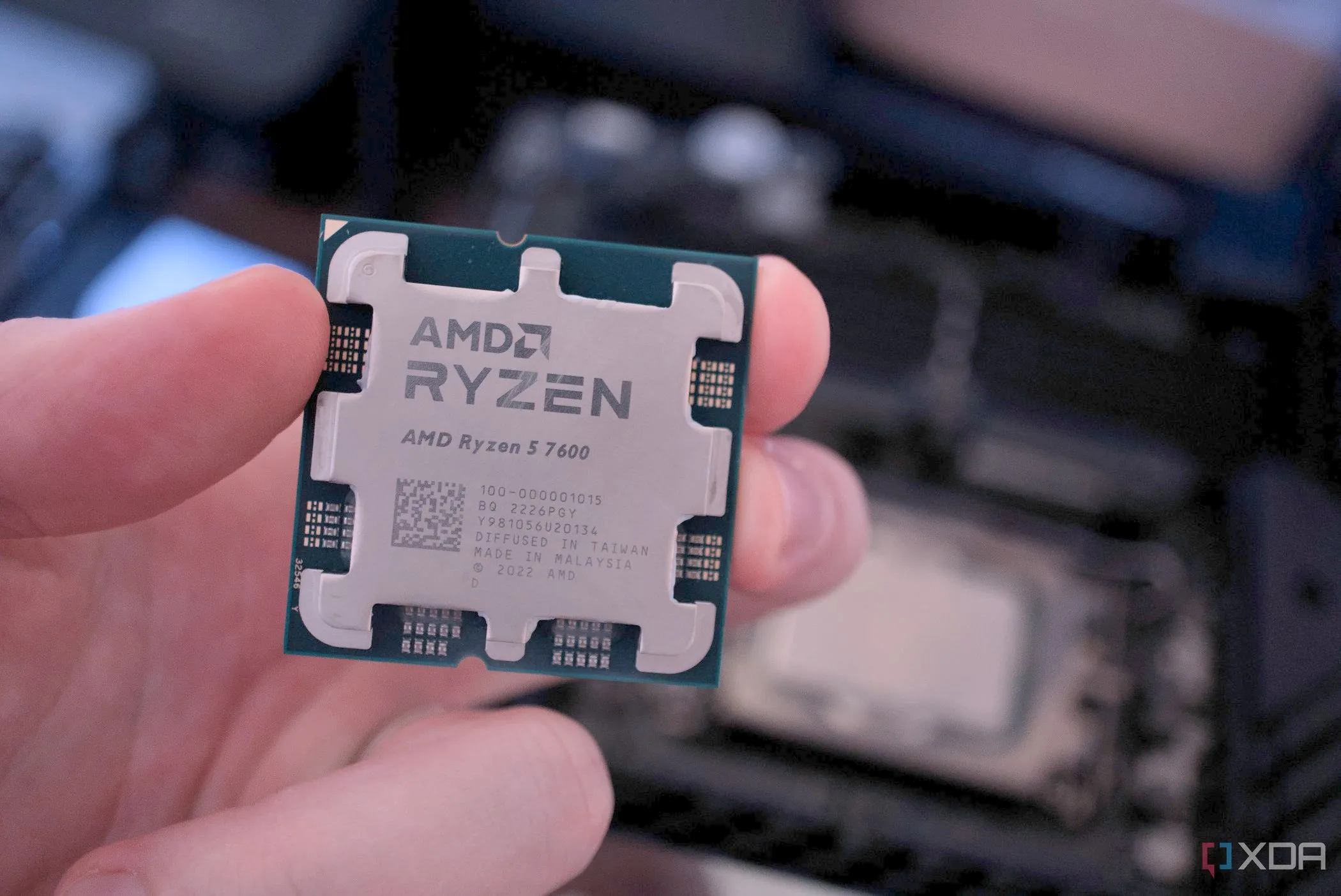 Bàn tay đang cầm hai bộ vi xử lý, một CPU AMD Ryzen 7 7700 và một CPU Intel, tượng trưng cho sự cạnh tranh trong thị trường chip