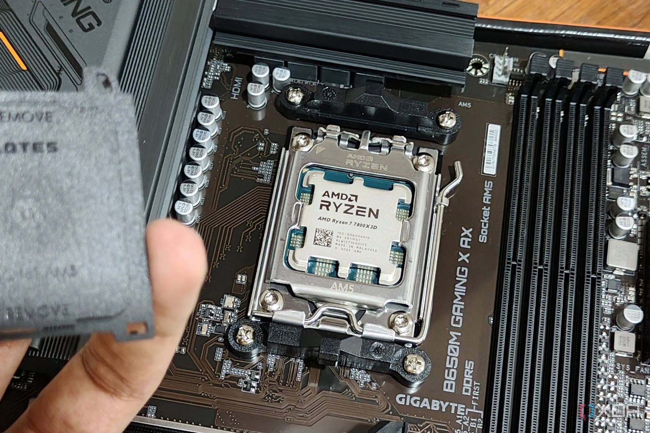 CPU AMD Ryzen 7 7800X3D được lắp trên bo mạch chủ, tay người dùng cầm nắp socket