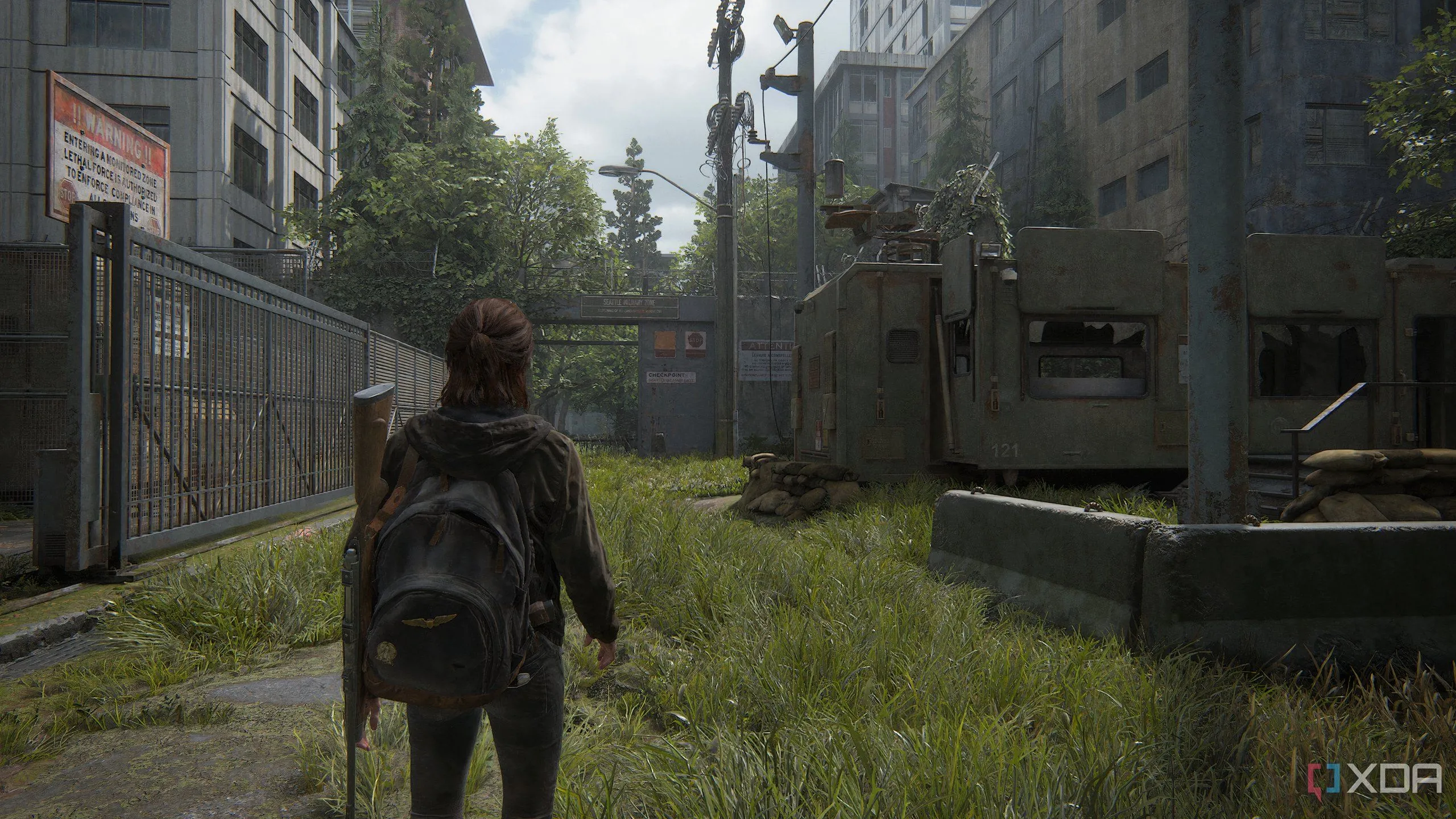 Ellie đi qua một khu phức hợp quân sự trong The Last of Us Part II Remastered trên PC, với đồ họa môi trường chi tiết và không khí căng thẳng.