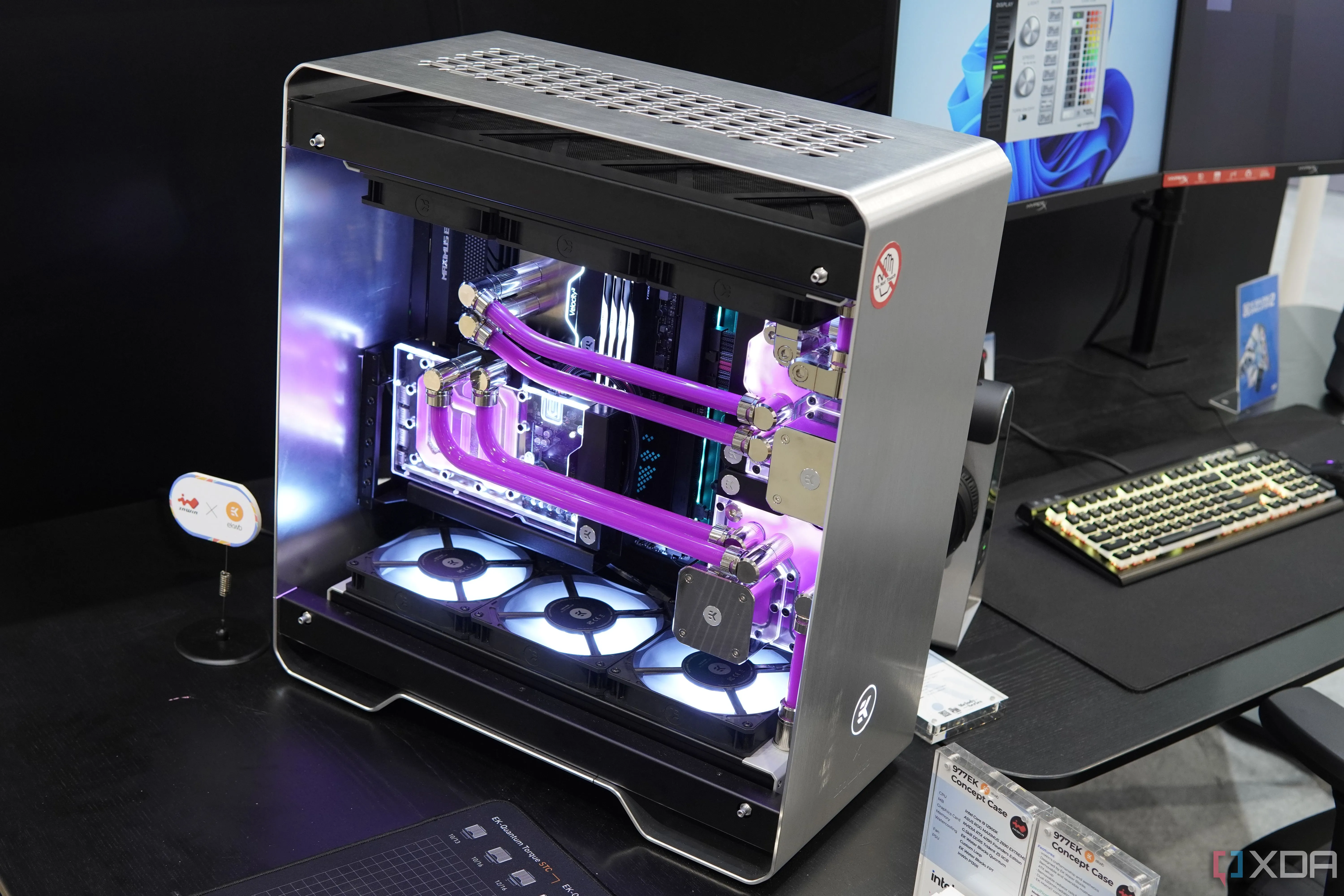 Góc nhìn xiên của bộ PC InWin 977EK tùy chỉnh với vỏ kim loại bạc và hai vòng tản nhiệt chất lỏng màu hồng, thể hiện một bản build PC được quản lý cáp chuyên nghiệp từ đầu