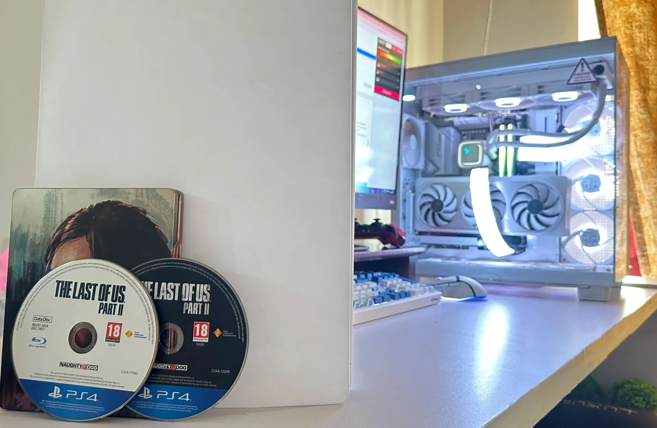 Hai đĩa game The Last of Us Part II phiên bản PS4 cùng với máy tính và PS5, minh họa kích thước game lớn.
