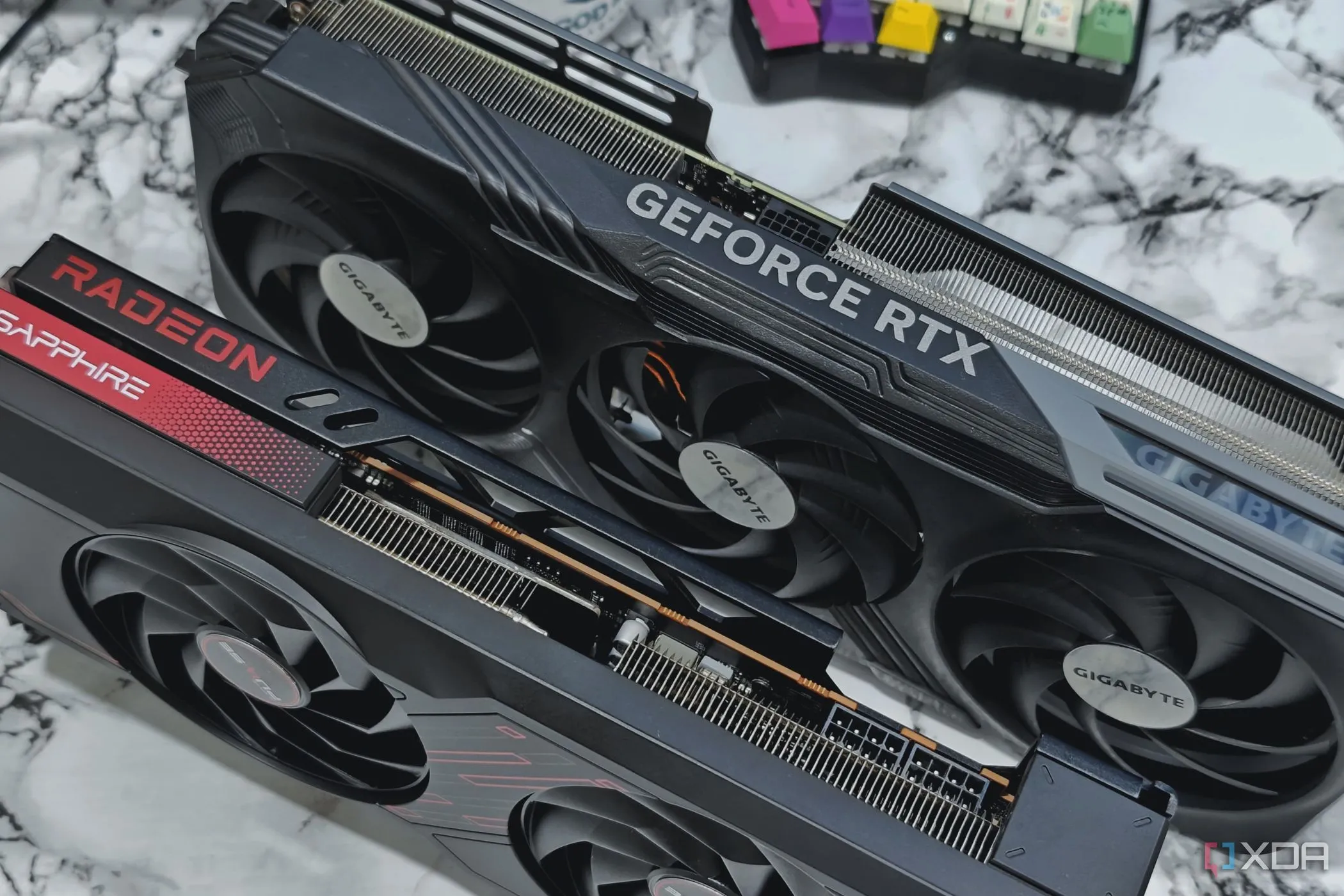 Hình ảnh cận cảnh hai card đồ họa GeForce RTX 4070 Ti và Radeon RX 7700XT đặt trên bàn cạnh một bàn phím cơ