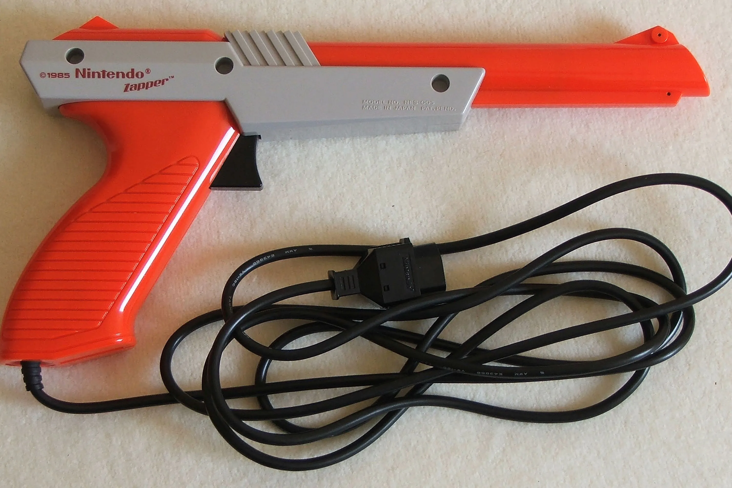 Khẩu súng NES Zapper màu xám đặt trên sàn, phụ kiện súng quang học huyền thoại của Nintendo cho game bắn súng cổ điển