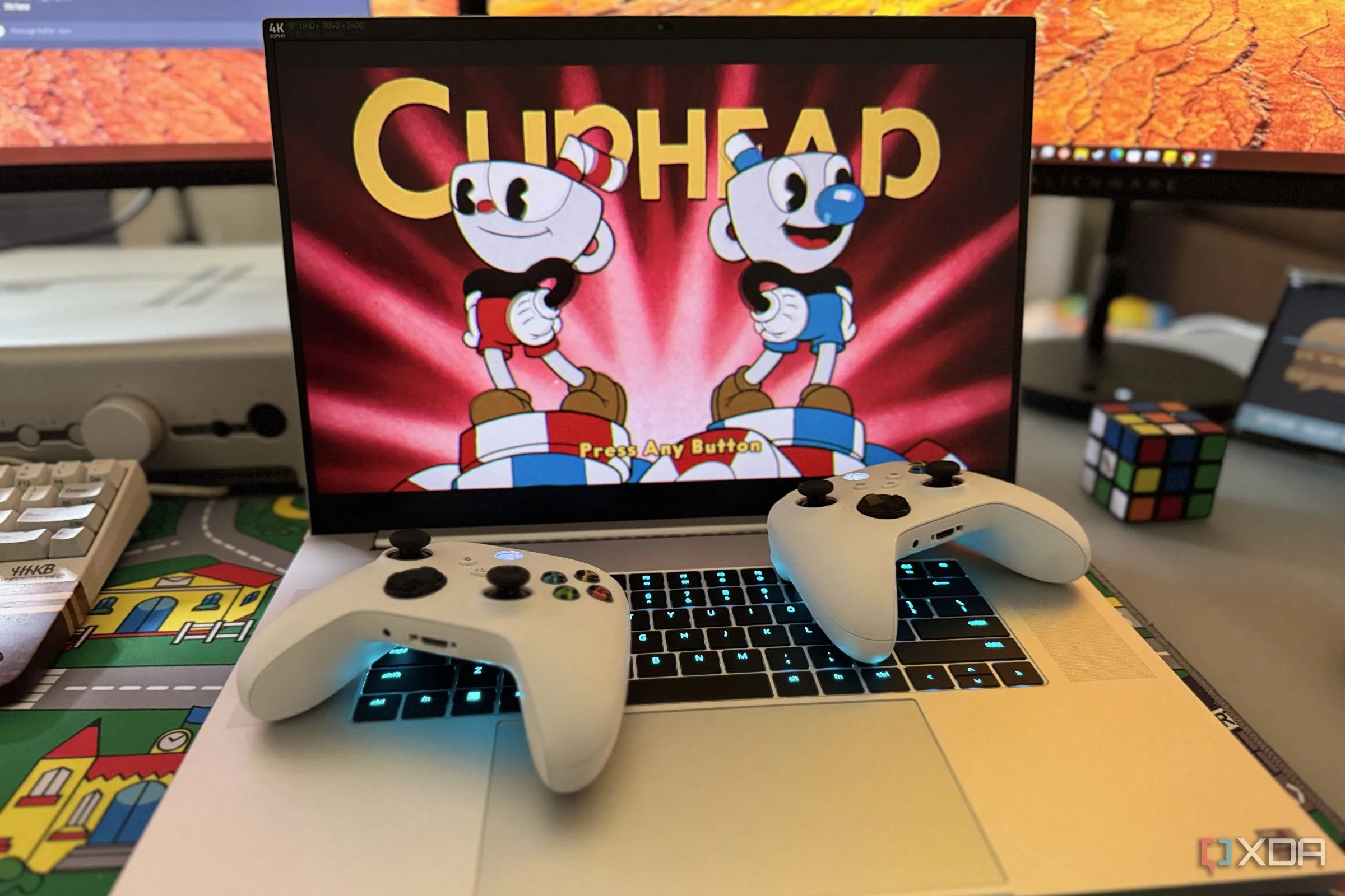 Laptop gaming Razer Blade 18 hiển thị game Cuphead, kèm hai bộ điều khiển Xbox trên bàn phím, minh họa trải nghiệm chơi game mượt mà sau khi tối ưu Windows