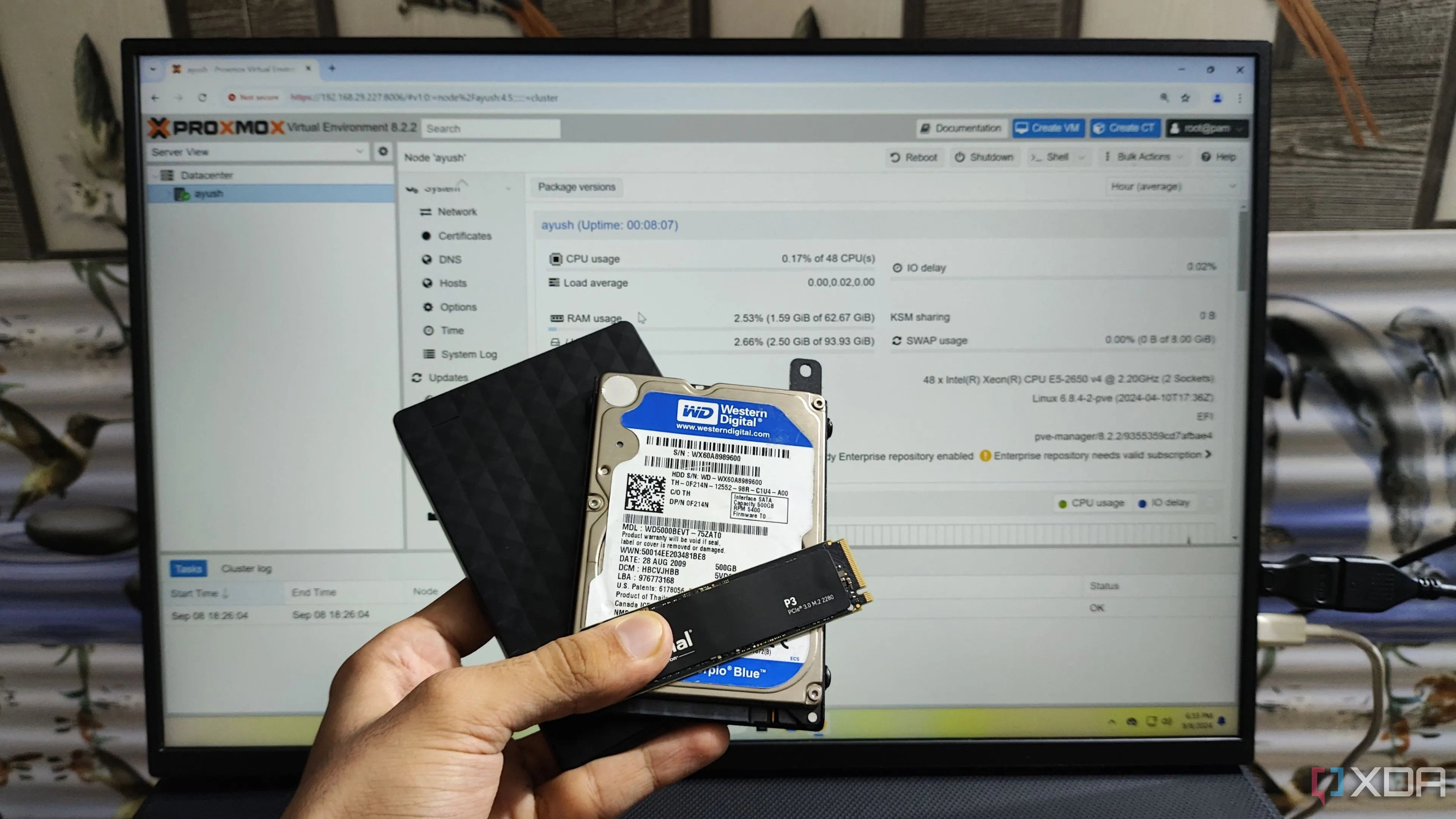 Một người đang cầm các loại ổ đĩa SSD, HDD và HDD gắn ngoài trước màn hình hiển thị giao diện Proxmox, thể hiện sự đa dạng trong quản lý phân vùng ổ cứng