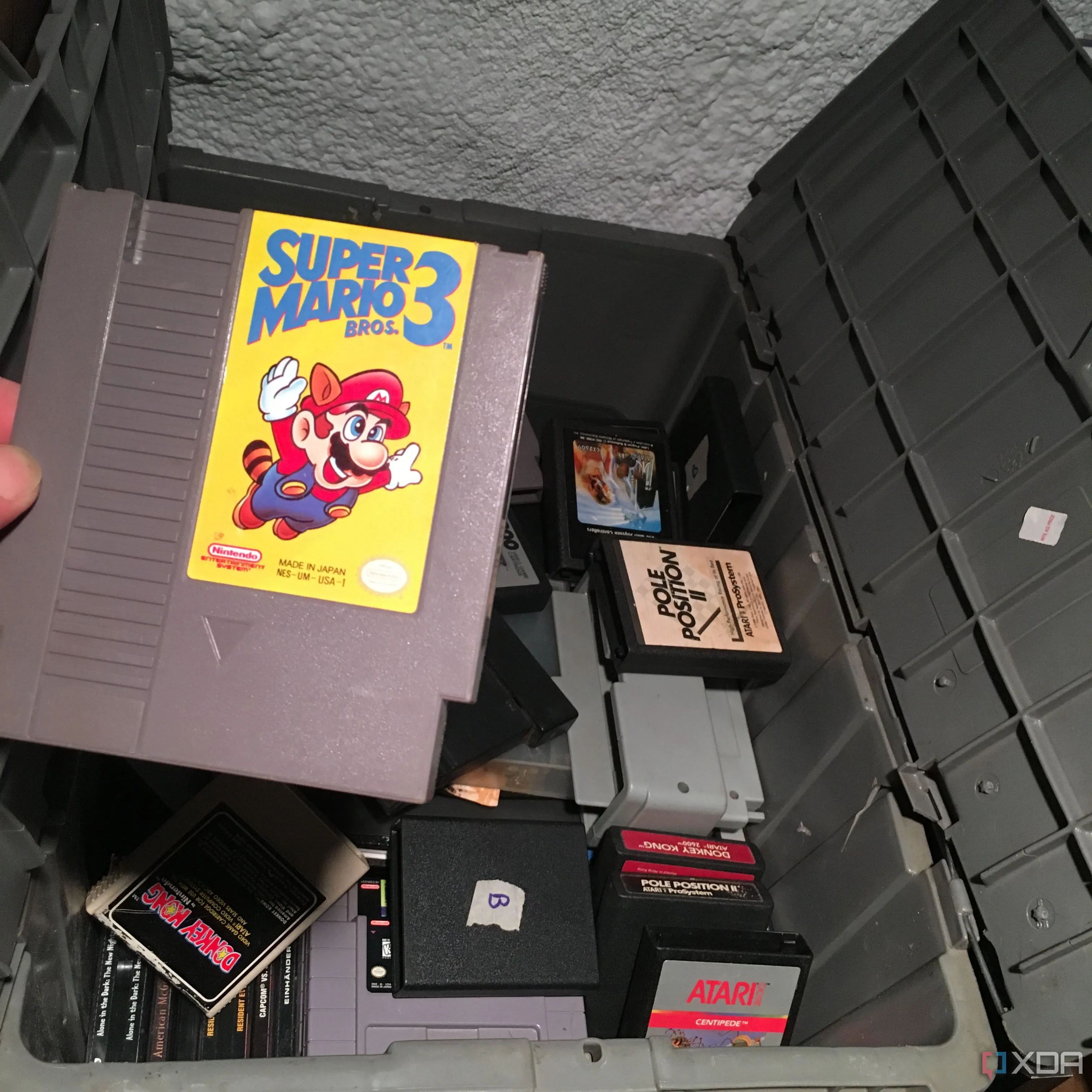 Người dùng đang lấy băng game Super Mario Bros 3 từ một hộp game retro cũ, tượng trưng cho việc khám phá lại những kỷ niệm và lịch sử gaming.