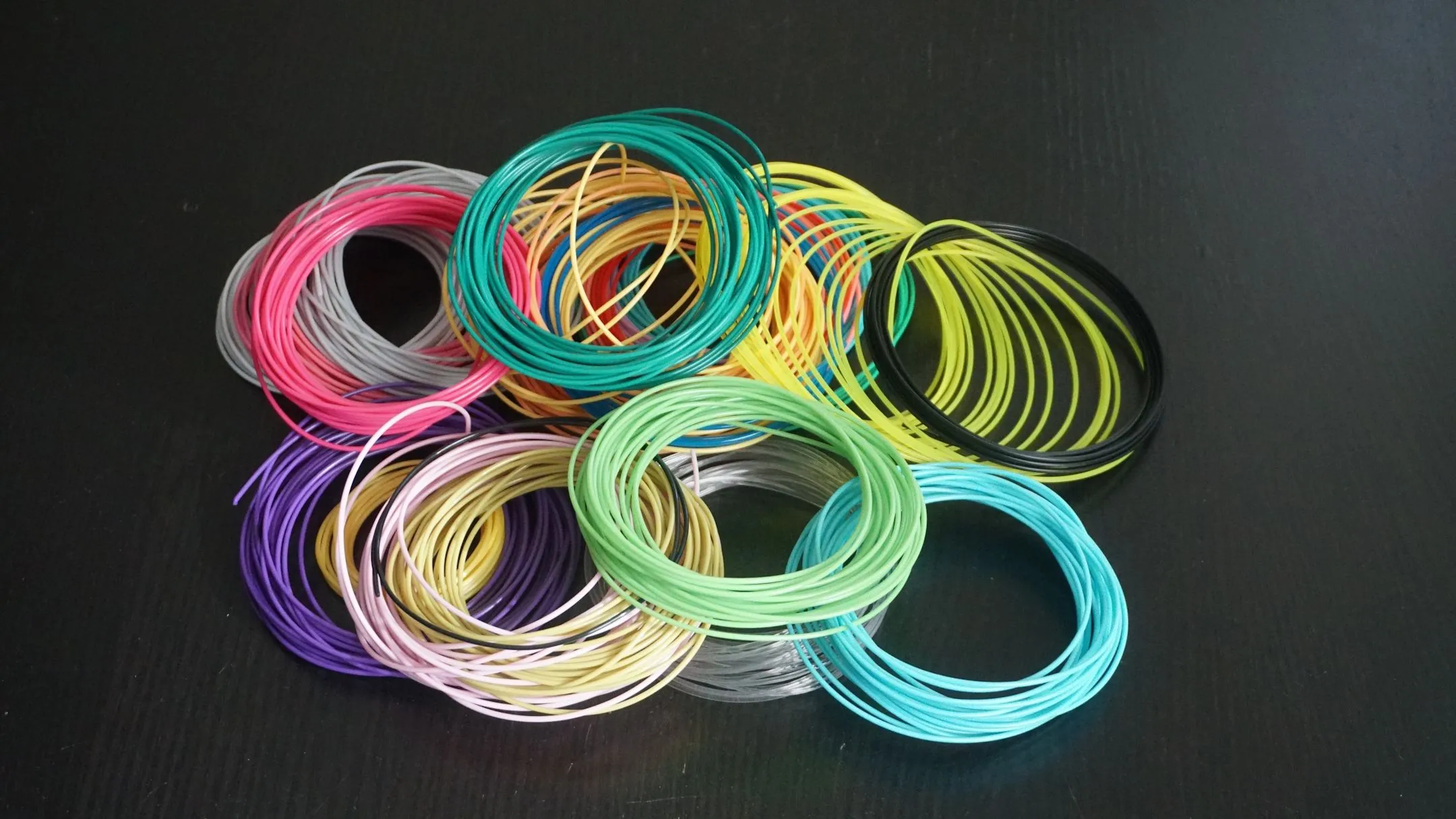 Nhiều cuộn sợi nhựa in 3D (filament) đủ màu sắc được xếp cạnh nhau, tượng trưng cho vật liệu in